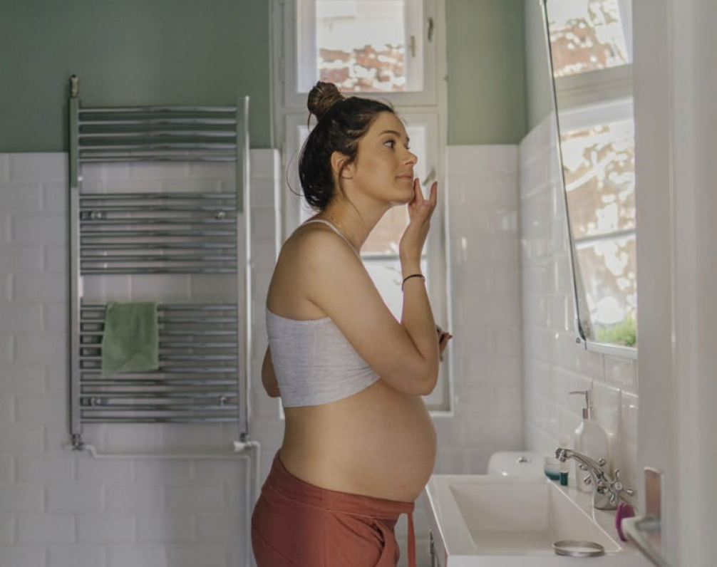 Pregnant woman smiling while applying face cream - pregnancy-safe skincare routine