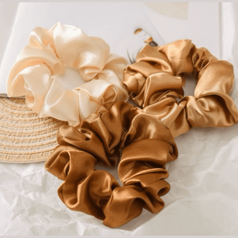Three beige and brown scrunchies on a white surface with a straw hat.