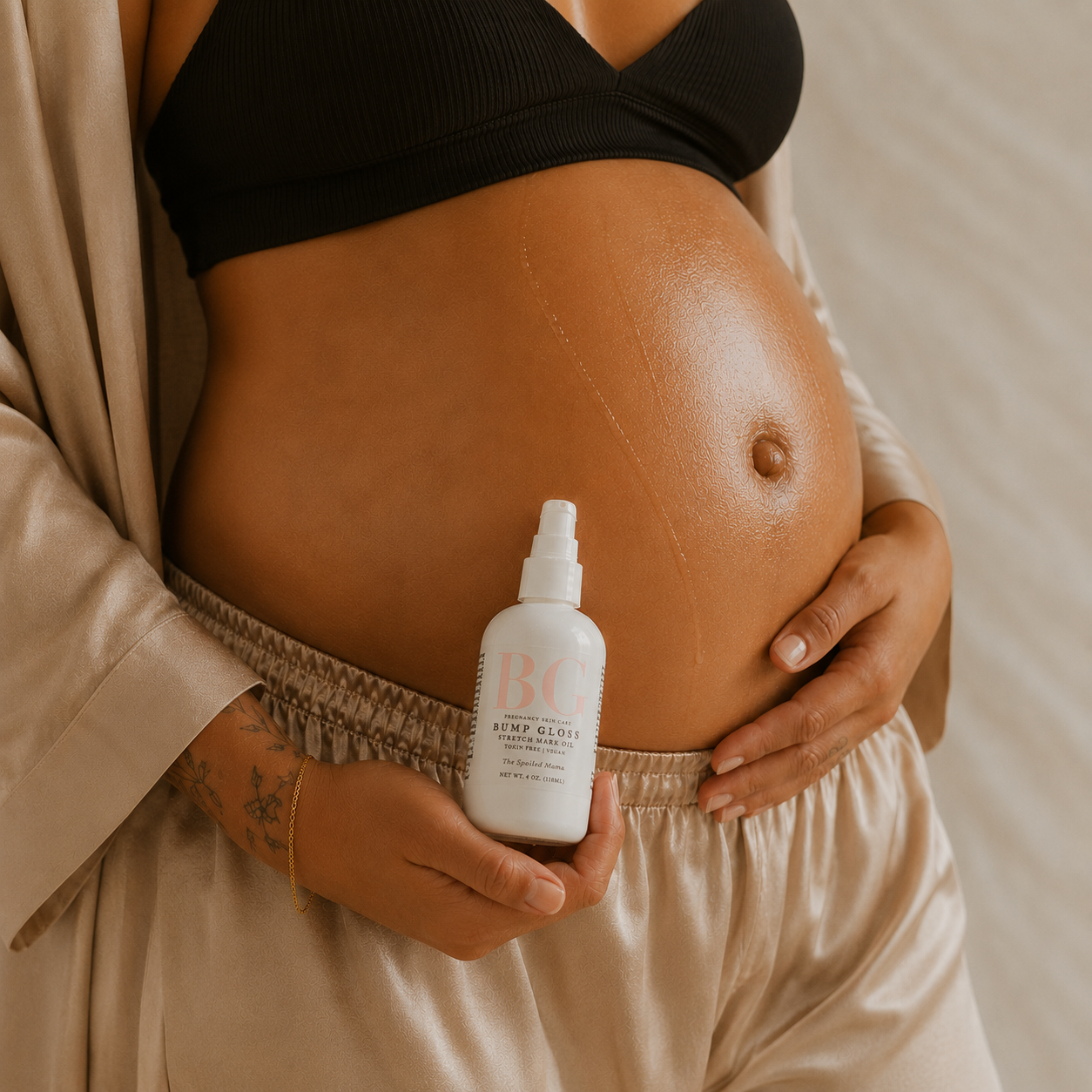 Pregnant woman rubbing in oil to belly and holding bump gloss bottle in silk pajamas