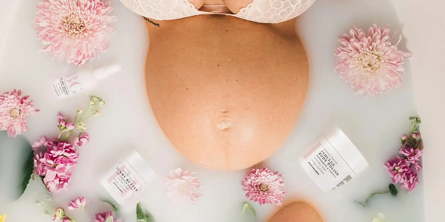 A pregnant woman is lying in a bathtub with pink flowers and OB-GYN-recommended skincare products.