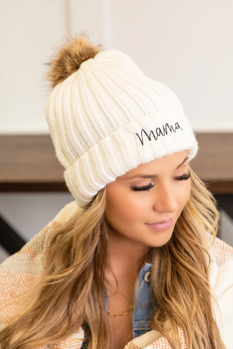 Woman wearing a white knit beanie with 'Mama' embroidery, indoors.