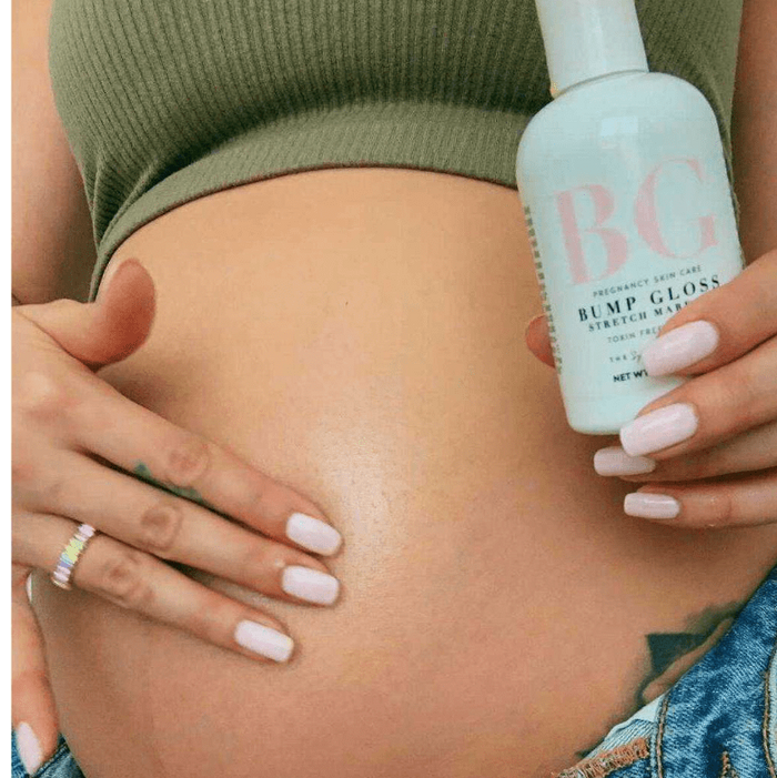 Pregnant mom holding a bottle of 'Bump Gloss' stretch mark oil against their stomach.