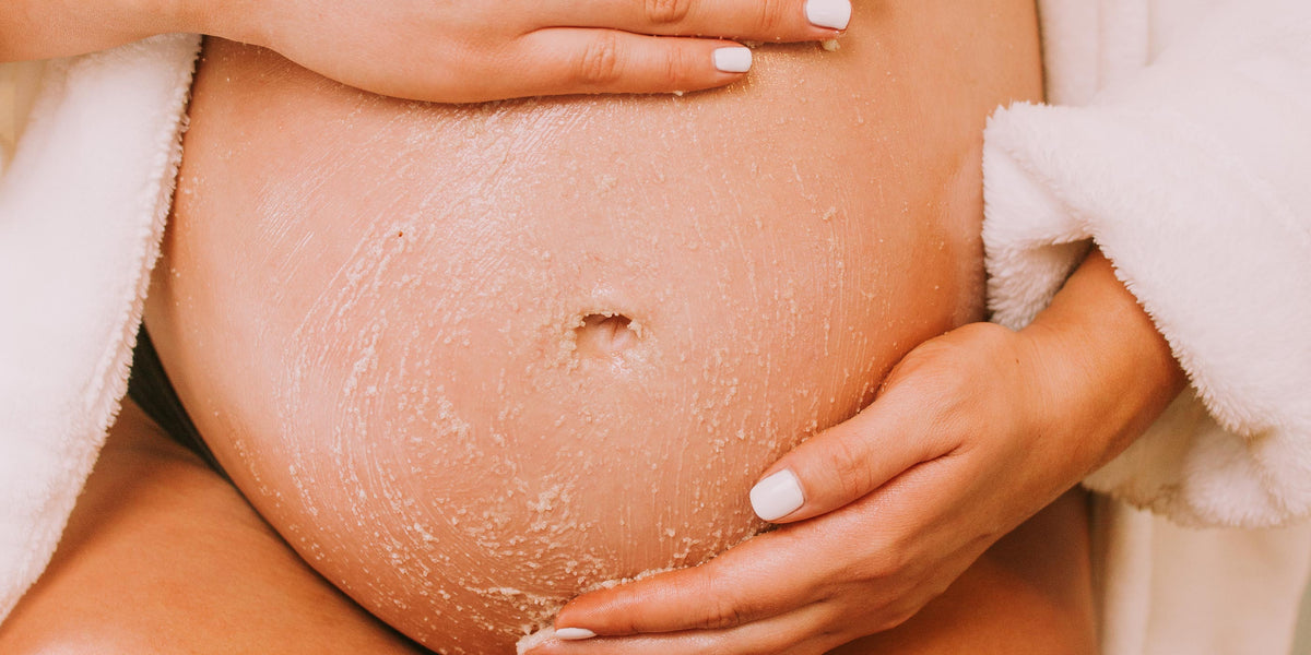 Pregnant woman in robe holding belly, showcasing OBGYN-recommended non-toxic skincare for pregnancy and postpartum