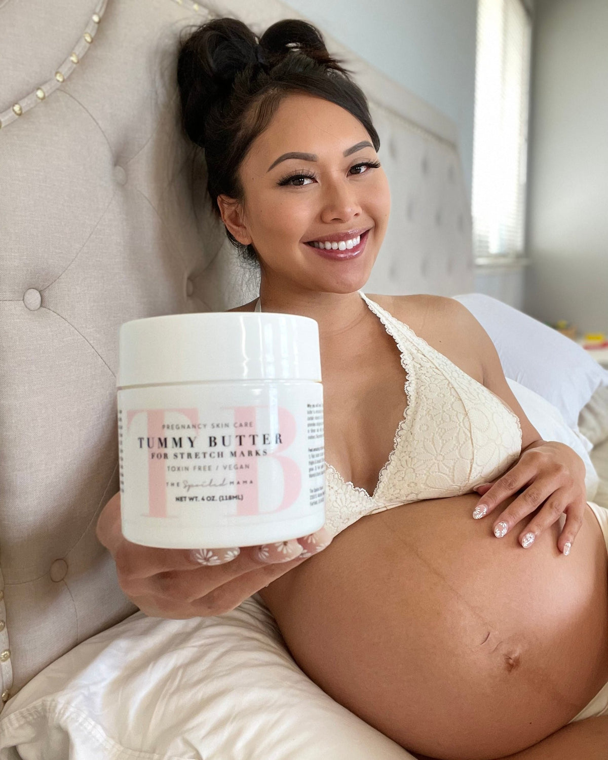 Pregnant mom in bed holding The Spoiled Mama Tummy Butter for stretch marks, 4 oz jar